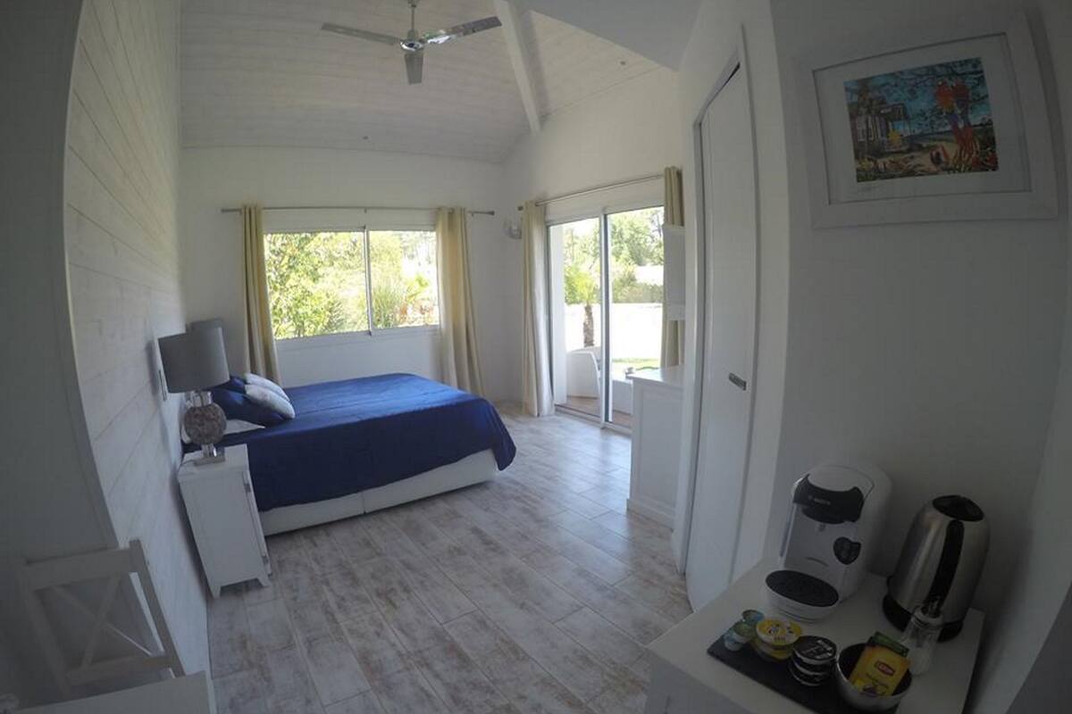 A bedroom with a bed, a bedside table, a lamp, a coffee maker, and a breakfast bar with food items.