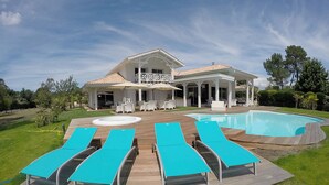 A large house with a pool, a covered patio, and lounge chairs. - Villa Bora Bora (Gujan-Mestras)