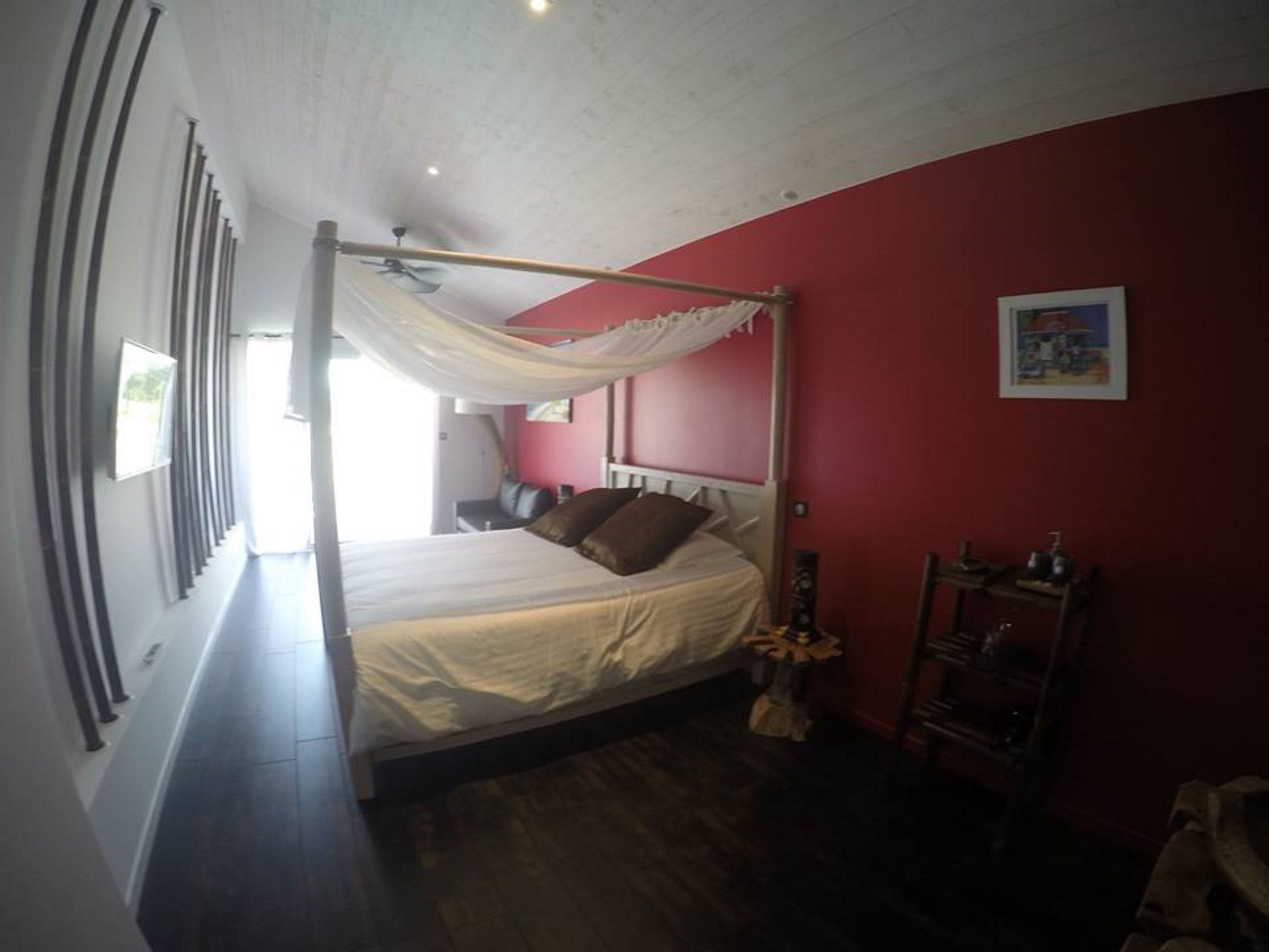 Une chambre à coucher avec un lit à baldaquin, un plancher en bois, un mur rouge et un ventilateur de plafond.