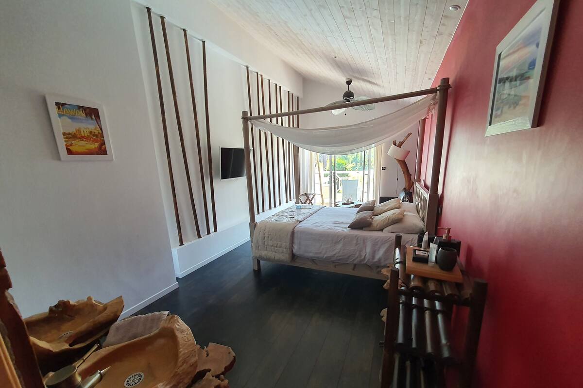 A bedroom with a bed, a ceiling fan, a TV, and a window with a view of the outdoors.