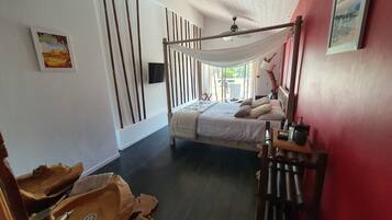 A bedroom with a bed, a ceiling fan, a TV, and a window with a view of the outdoors.
