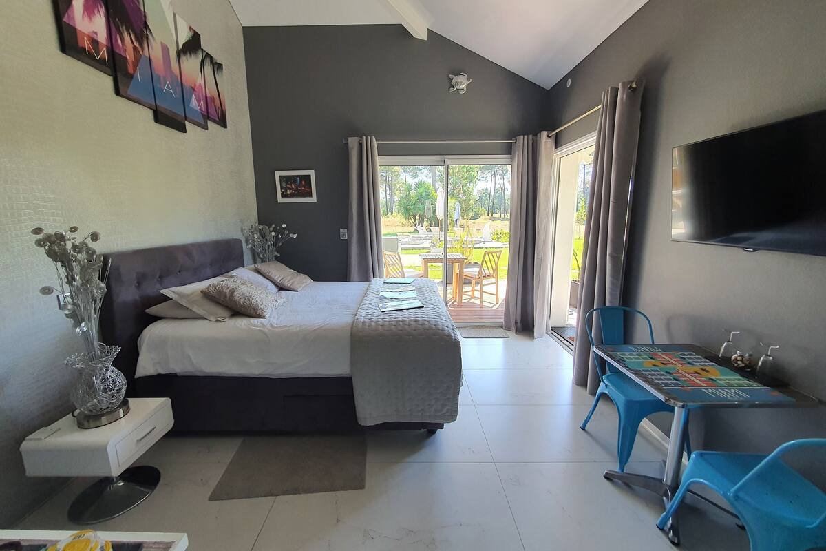 A bedroom with a bed, a desk with a chair, a TV, and a view of the outdoors.