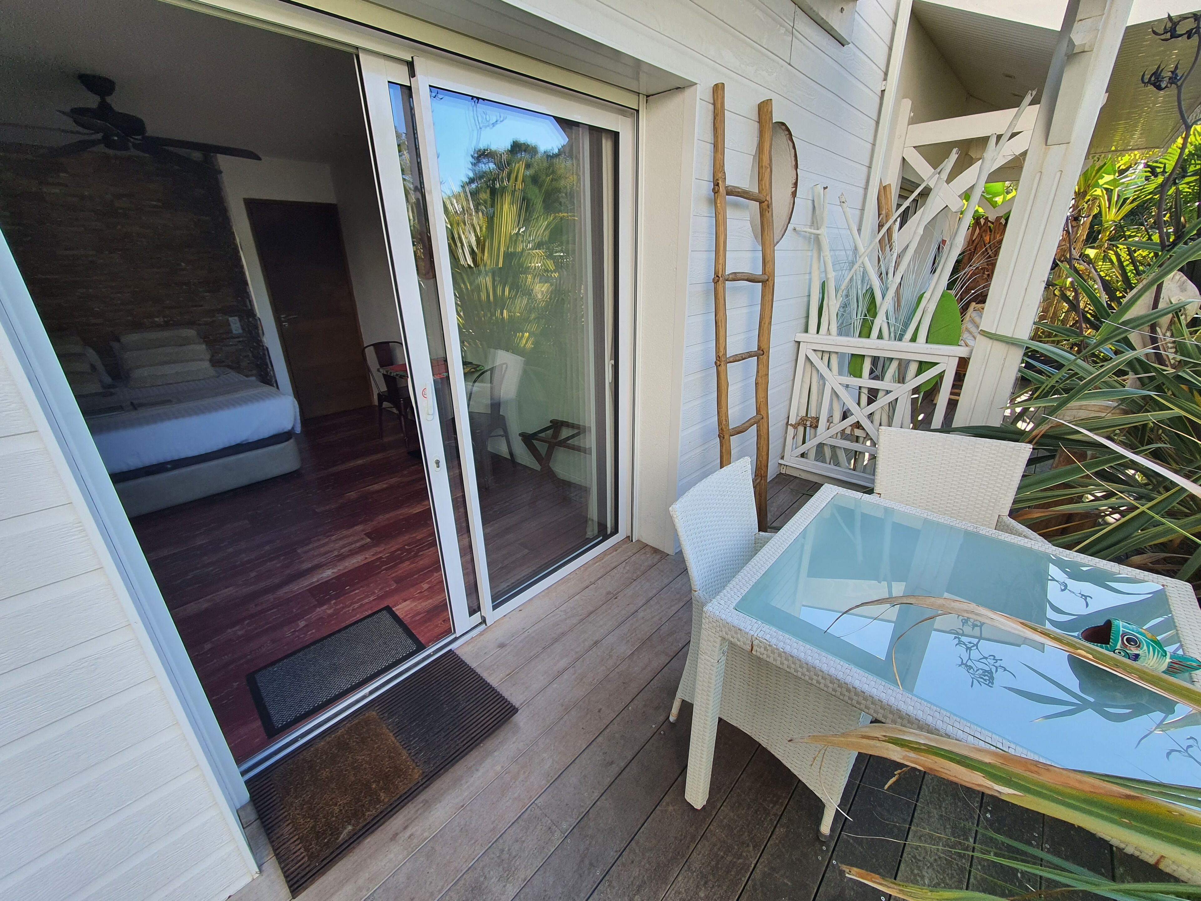 Een balkon met een glazen tafel, rieten stoelen, een houten ladder en uitzicht op het interieur.