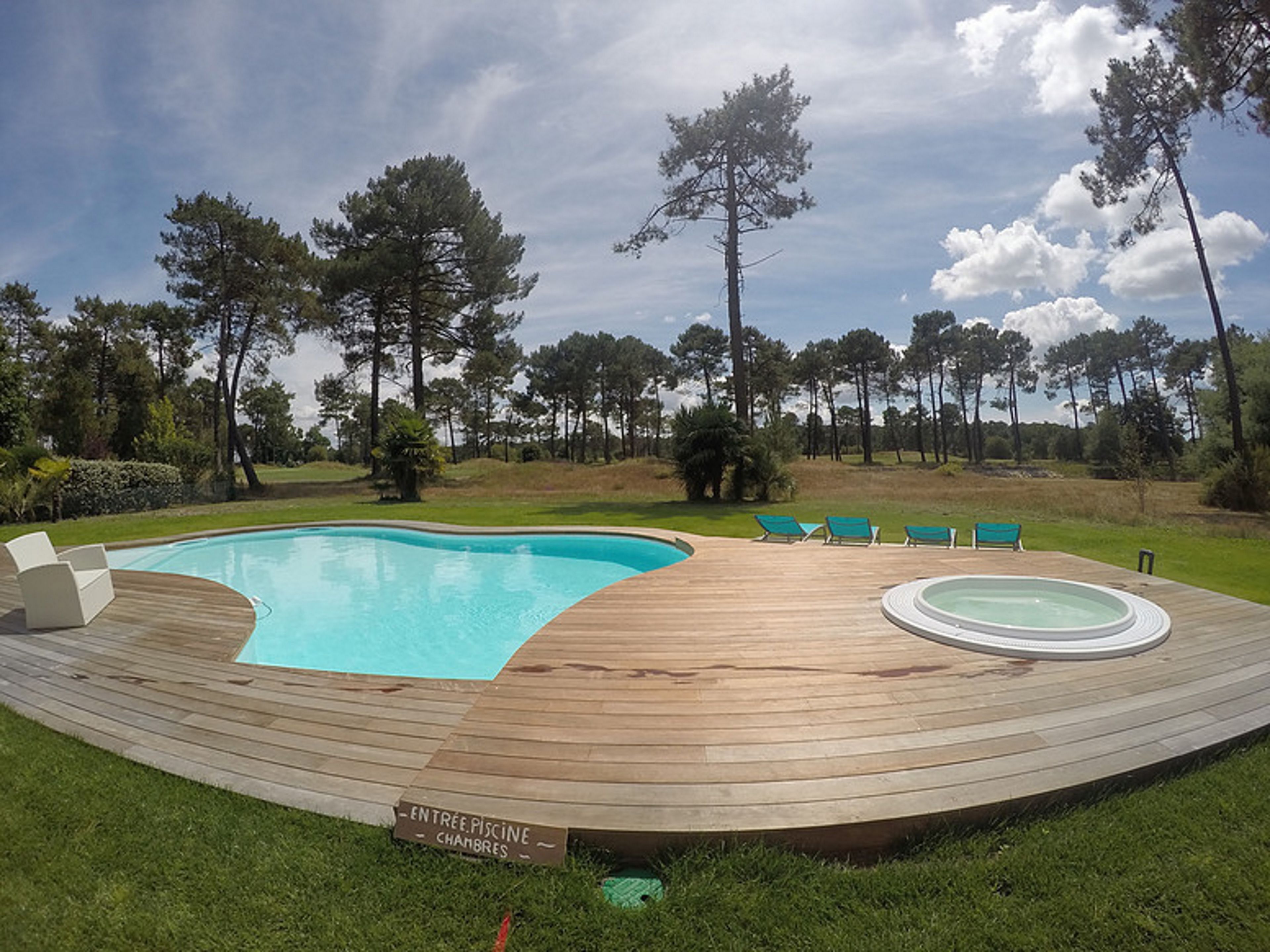A swimming pool with a wooden deck, lounge chairs, and hot tubs.