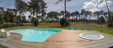 A swimming pool with a wooden deck, lounge chairs, and hot tubs.