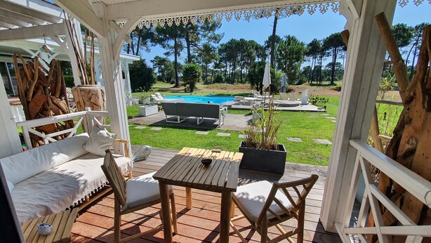A covered outdoor area with a wooden deck, seating, and a view of a swimming pool. - Villa Bora Bora (Gujan-Mestras)