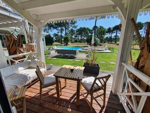 A covered outdoor area with a wooden deck, seating, and a view of a swimming pool. - Villa Bora Bora (Gujan-Mestras)