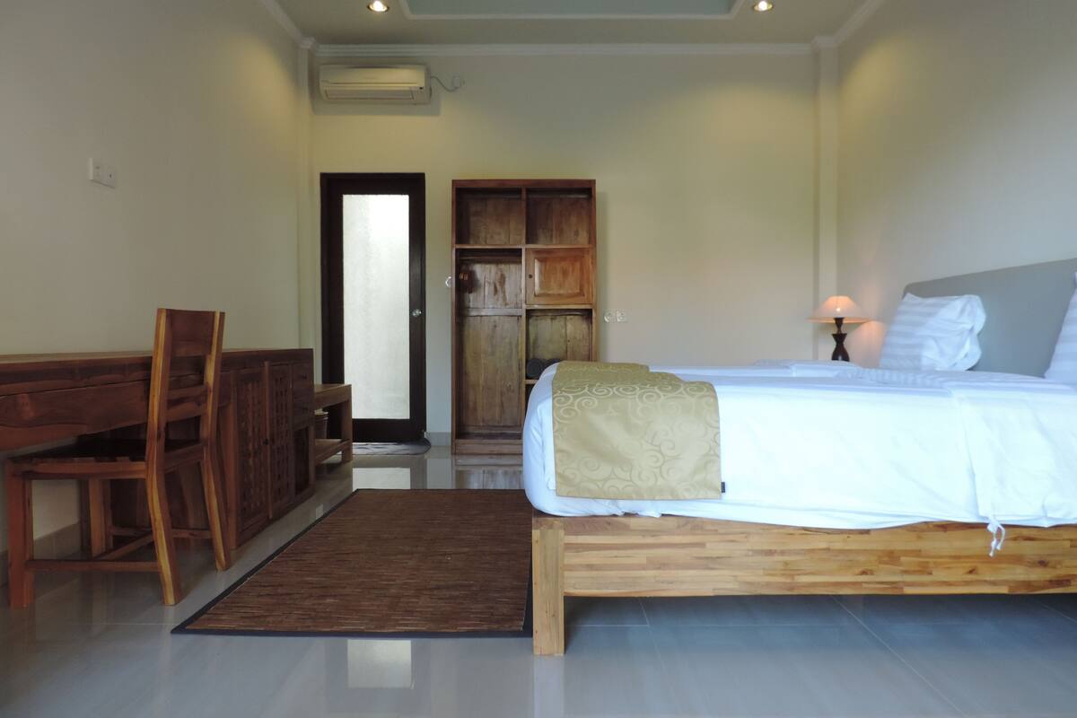 A bedroom with a bed, wooden headboard, bedside table, lamp, and a wooden wardrobe.