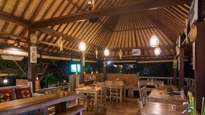 Un comedor interior con mesas y bancos de madera, lámparas colgantes y un techo de paja.