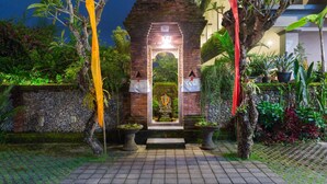 Una estructura que recuerda a un templo, con una estatua central, rodeada de plantas en macetas y un muro de piedra con máscaras.