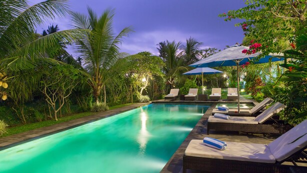 Piscina con sillas de descanso y sombrillas, rodeada de vegetación tropical.