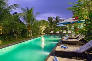 A swimming pool with lounge chairs and umbrellas, surrounded by tropical vegetation. - Kiskenda Cottages (Ubud)