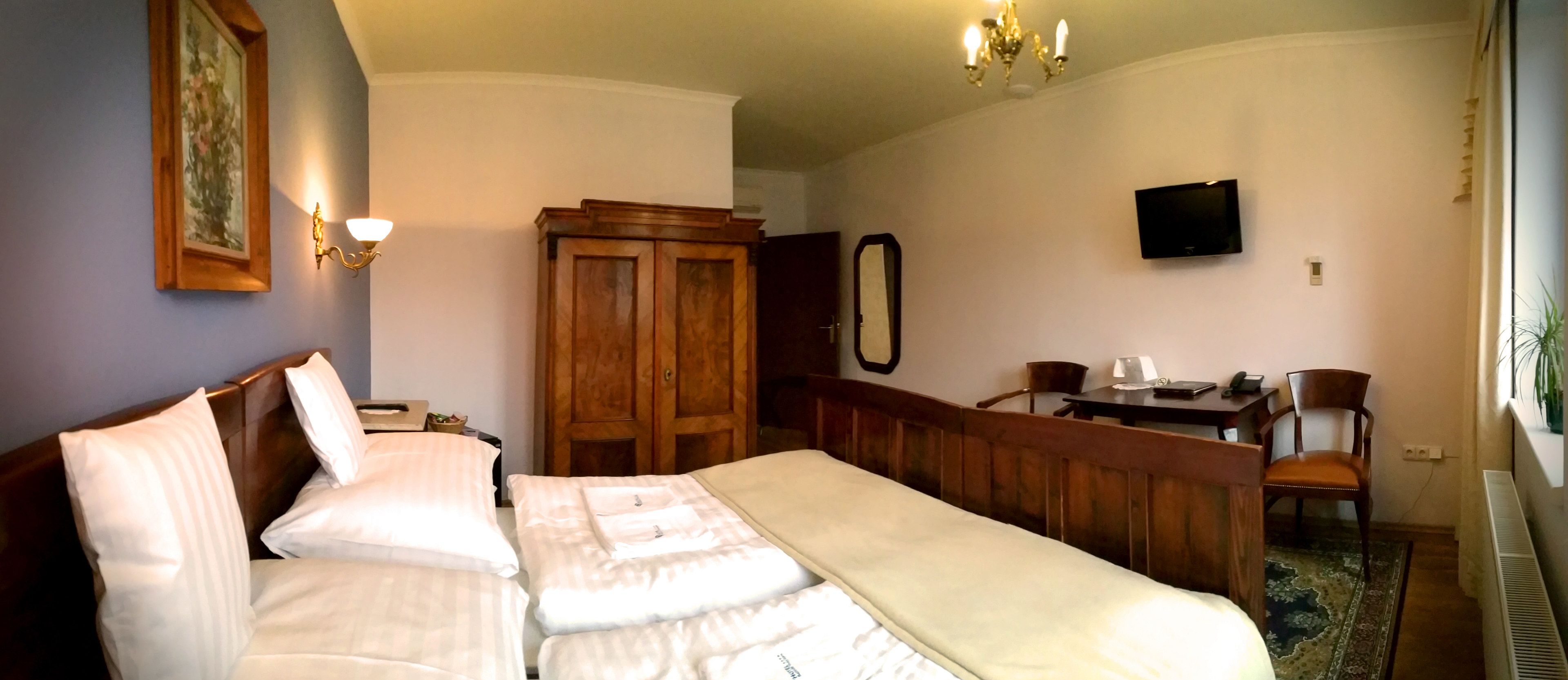 A hotel room with a bed, a desk, a chair, a television, and a wardrobe.