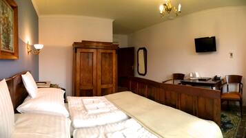 Quarto de hotel com cama, escrivaninha, cadeira, televisão e guarda-roupa.