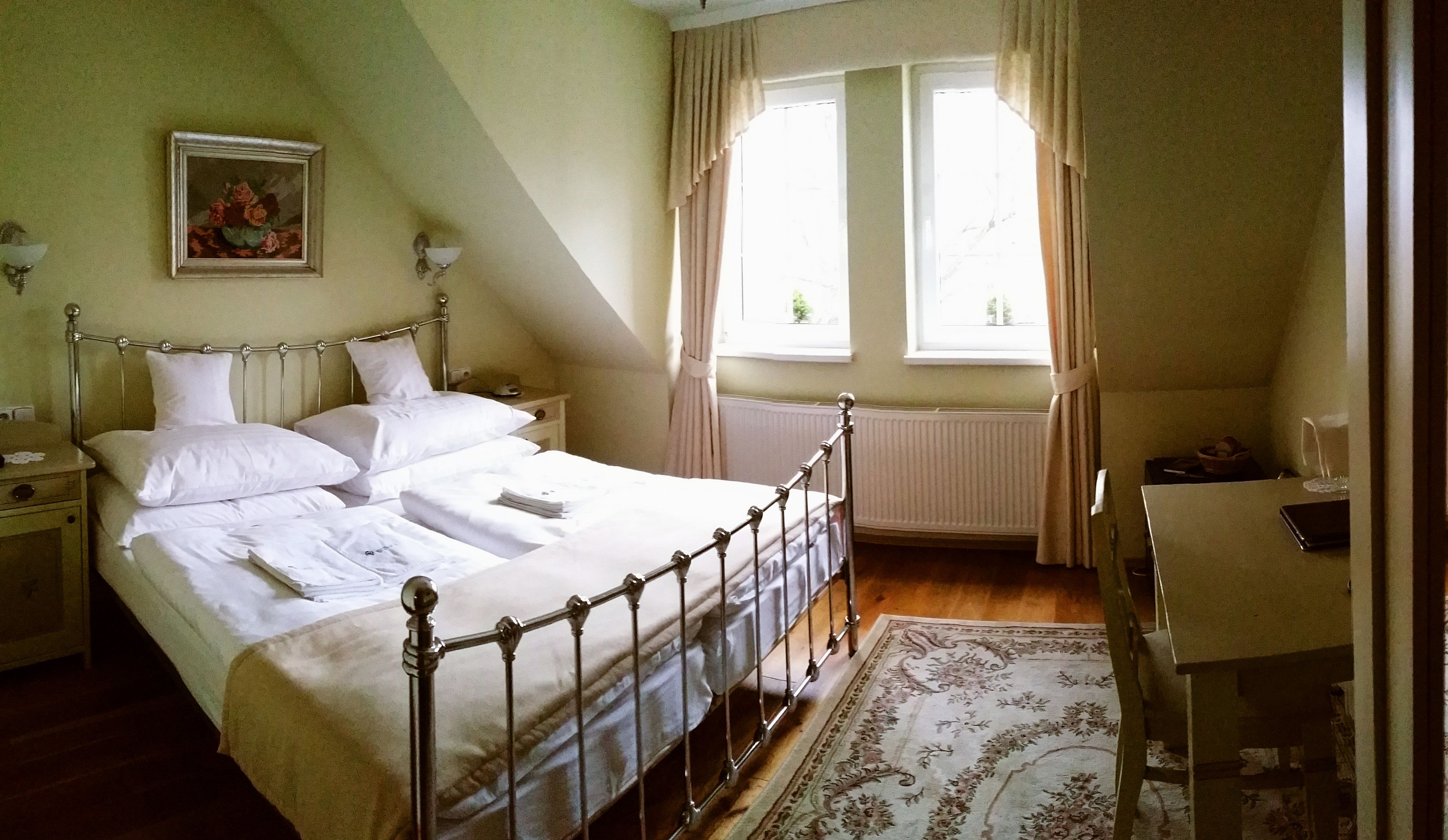 A neatly made bed in a room with a window, a bedside table, and a chair.