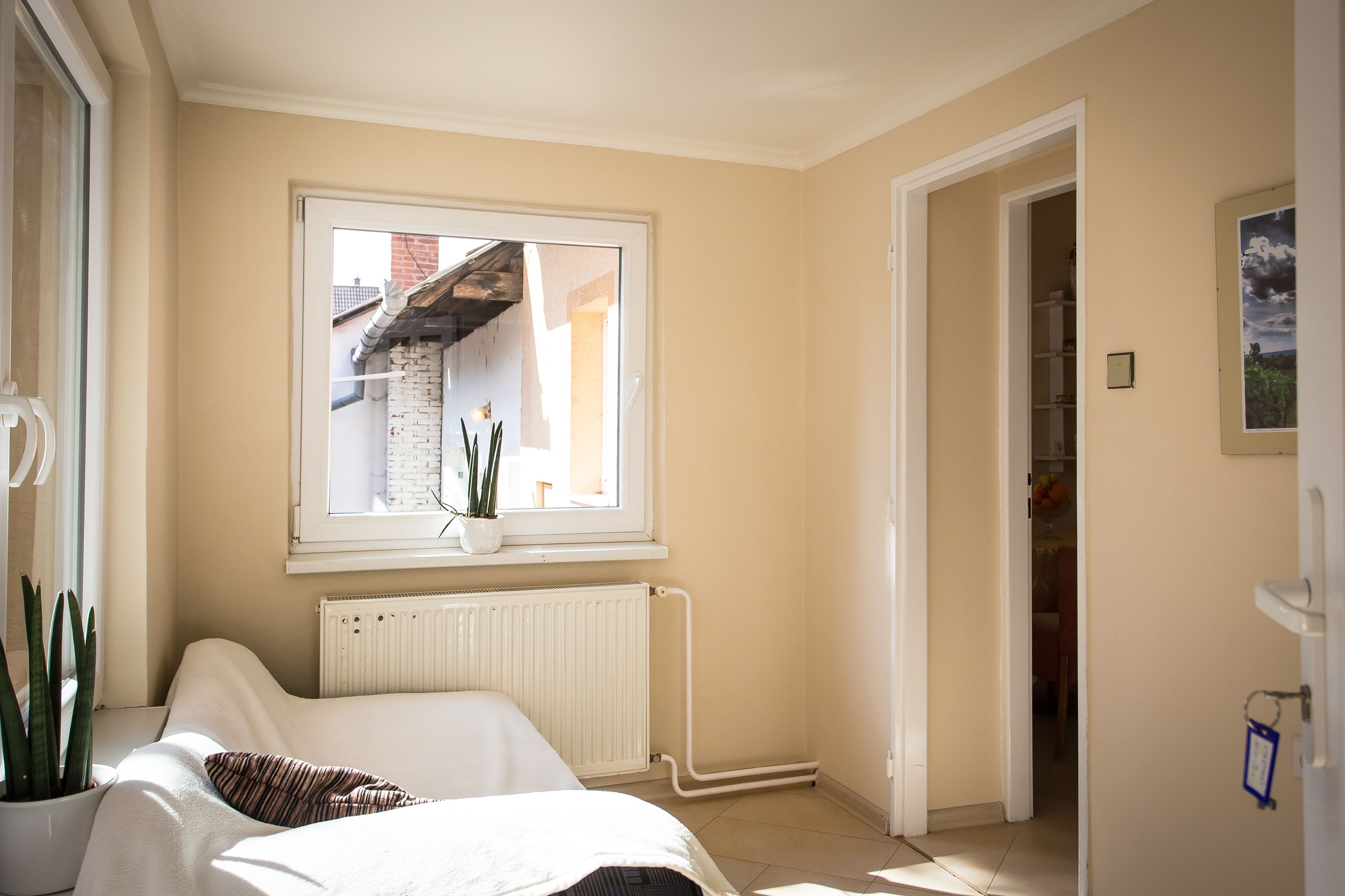 A bedroom with a bed, a radiator, a window with a view of a brick building, and a door leading to another room.
