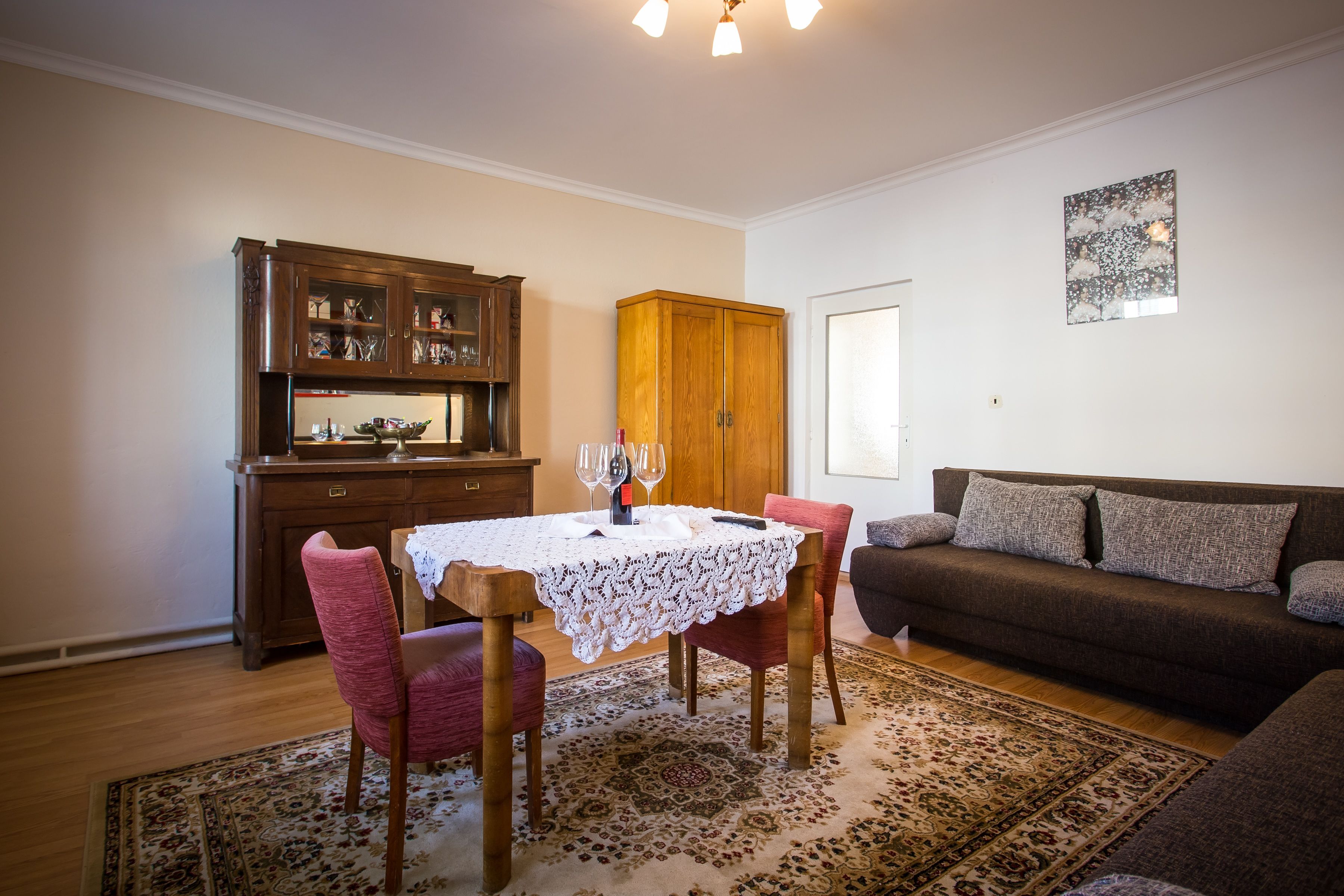 A dining area with a table set for four, a wooden cabinet, a sofa, and a patterned rug.