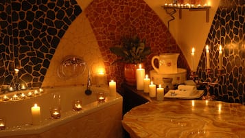 A bathroom with a stone mosaic wall, a bathtub with candles, a sink, and a mirror.