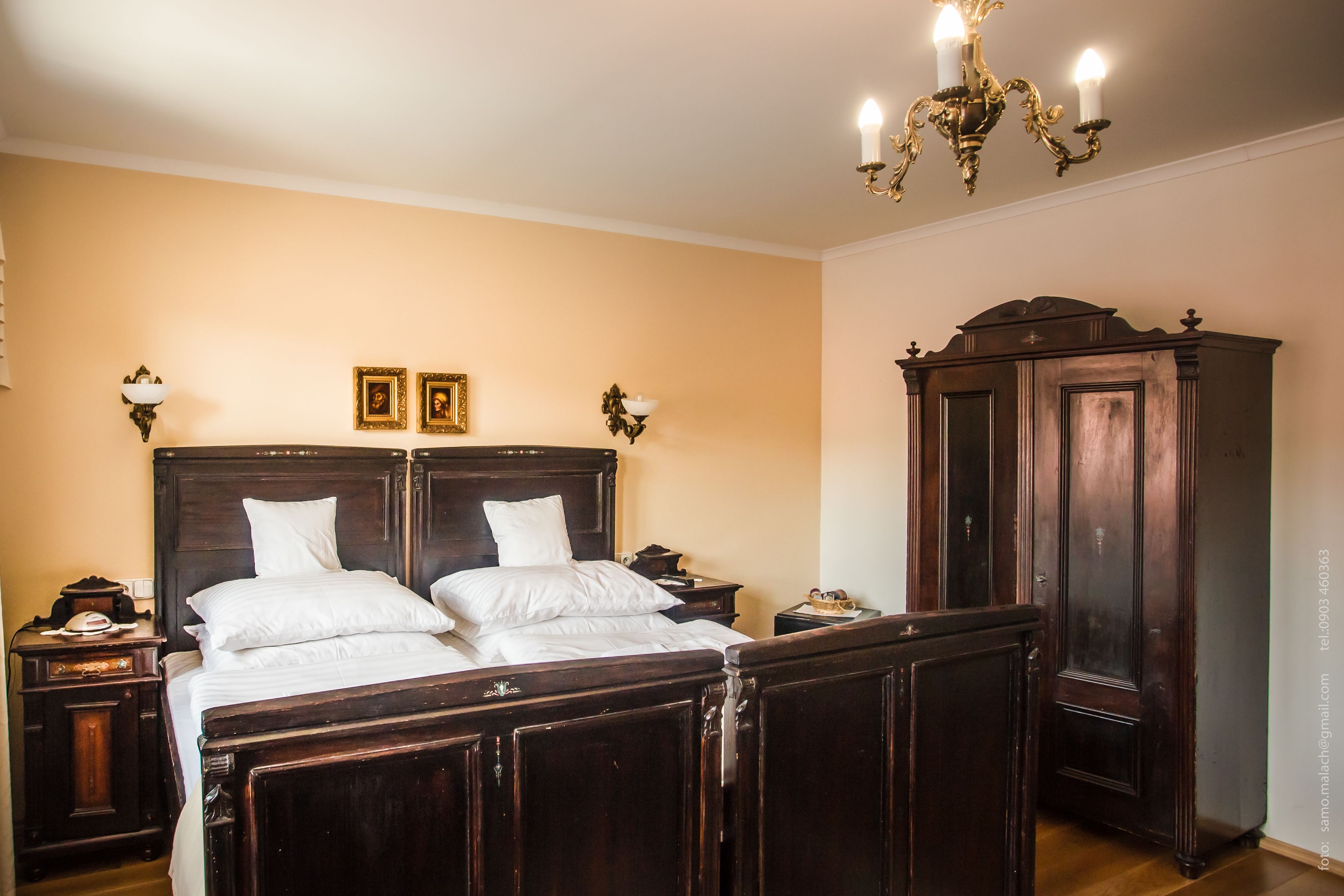 A bedroom with a large wooden bed, two bedside tables, a wardrobe, and a chandelier.