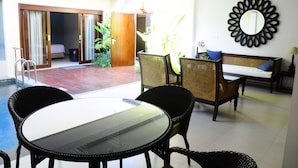 A hotel room with a glass table, wicker chairs, a sofa, and a large mirror on the wall. - Puri Mesari Suites (Denpasar)