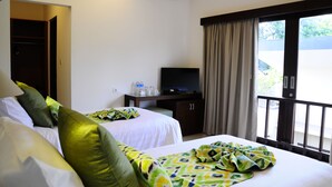 A hotel room with two beds, a TV on a wooden cabinet, an air conditioning unit, and a balcony with curtains. - Puri Mesari Suites (Denpasar)