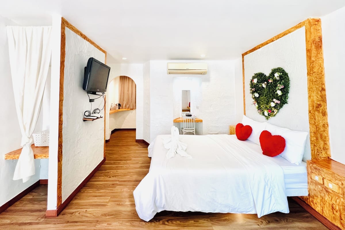 Een hotelkamer met een bed, een televisie, een spiegel, een bureau en een hartvormige decoratie aan de muur.