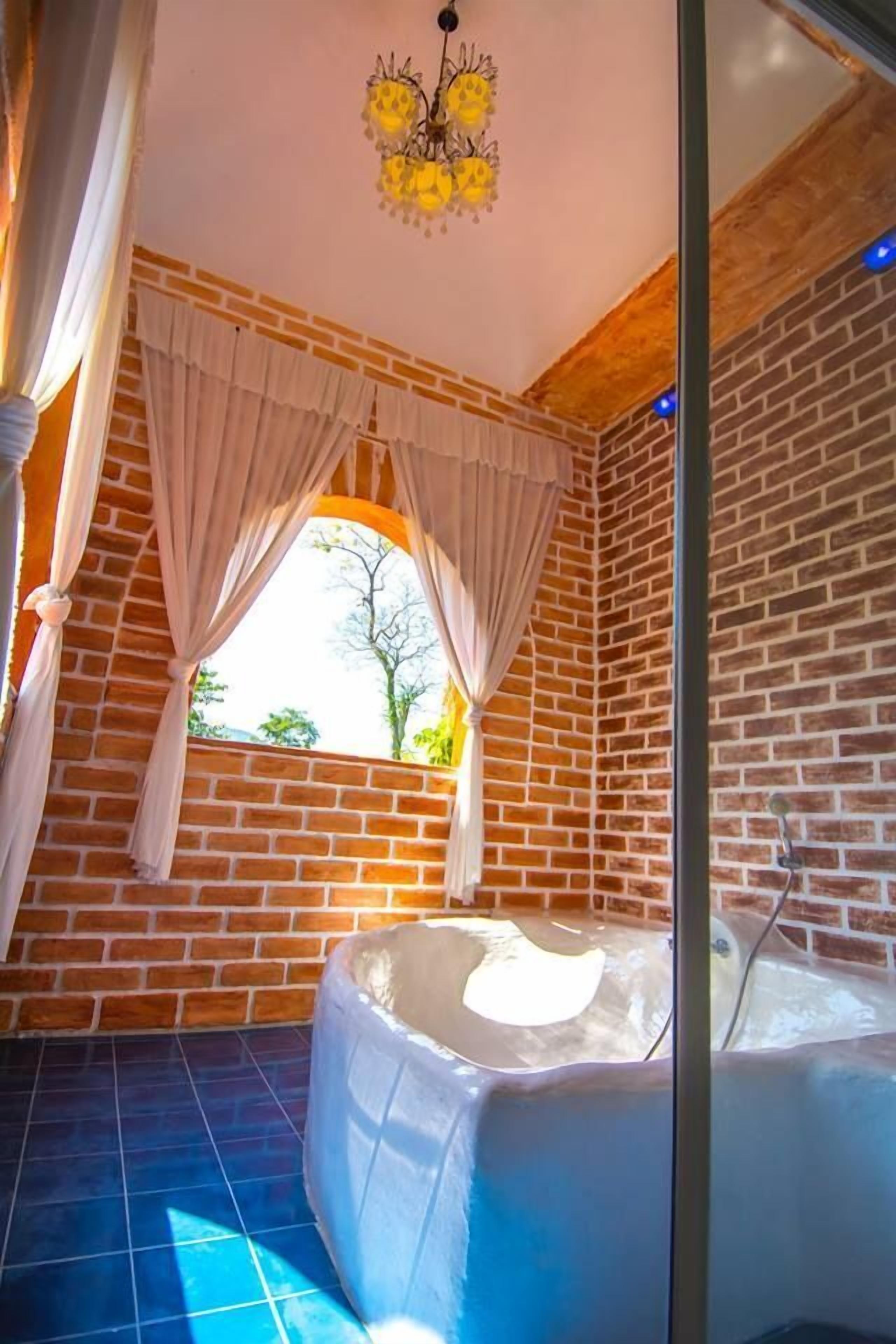 Een spa-ruimte met een bakstenen muur, een groot raam met gordijnen, een whirlpool en een kroonluchter.