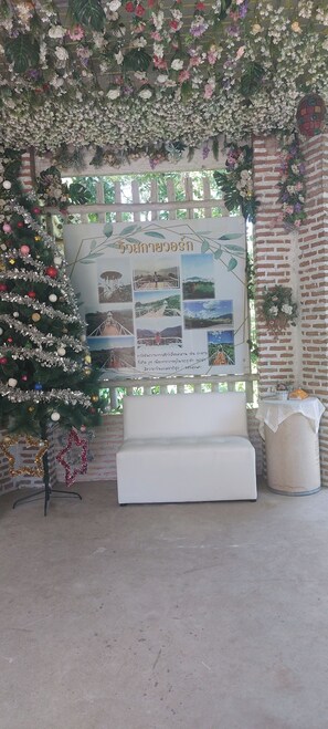Un espacio interior decorado con un banco blanco, un árbol de Navidad y un tablón de anuncios con fotos y texto.