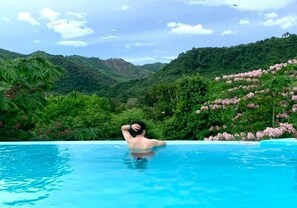 Uma pessoa relaxando em uma piscina com vista para vegetação exuberante e colinas.