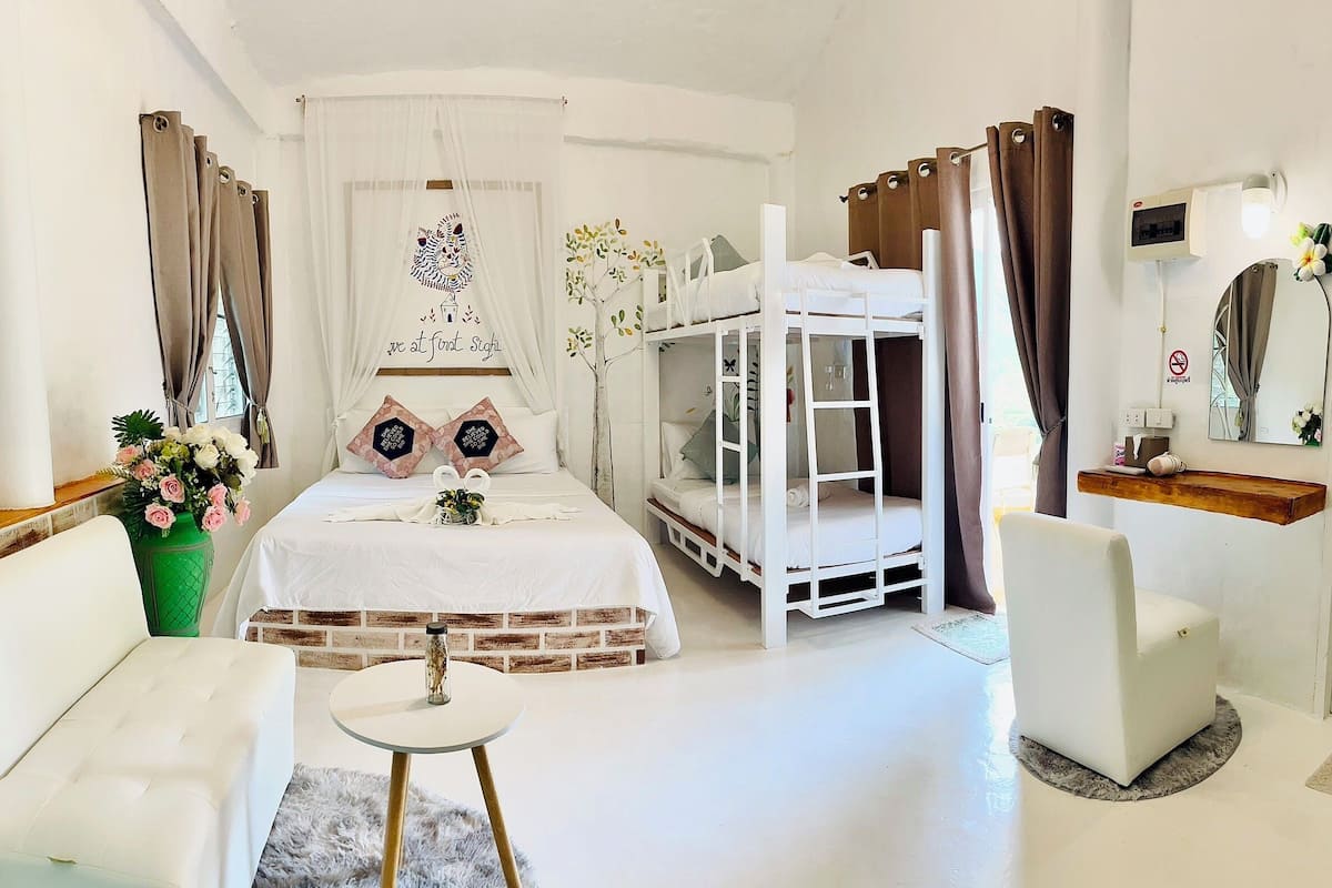 Een hotelkamer met een bed, stapelbedden, een slaapbank, een klein tafeltje en een spiegel.