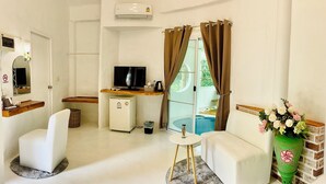 Een moderne kamer met een flatscreen televisie, een kleine koelkast, een bank, een bijzettafeltje en een groene vaas met bloemen.
