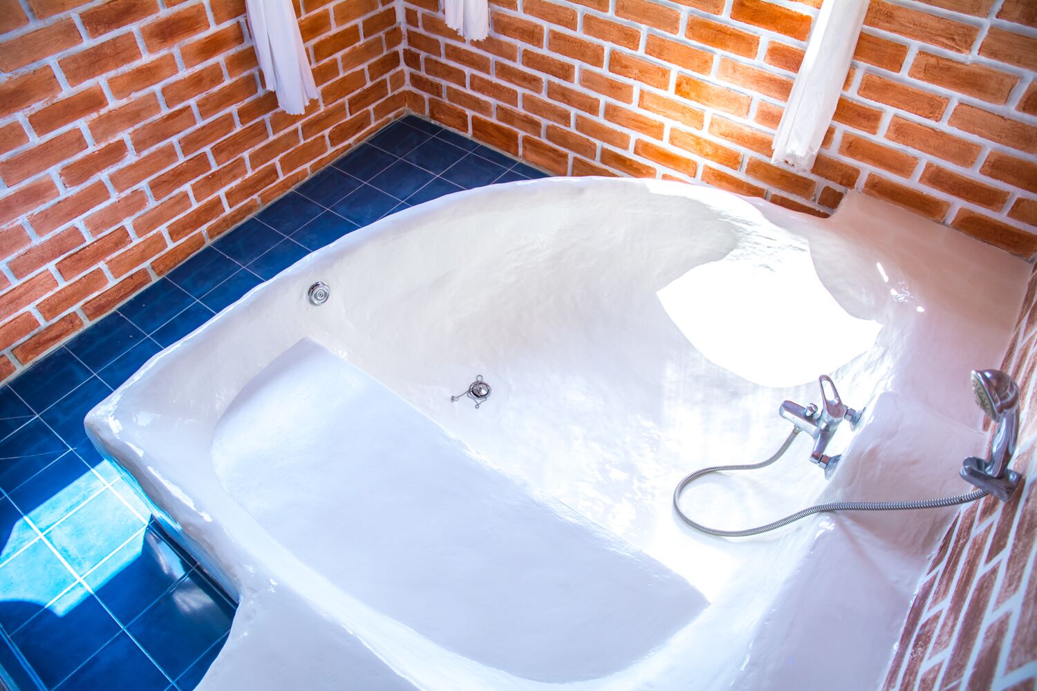 Un baño con una bañera blanca, azulejos azules y una pared de ladrillo.