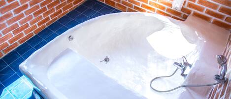 Un baño con una bañera blanca, azulejos azules y una pared de ladrillo.
