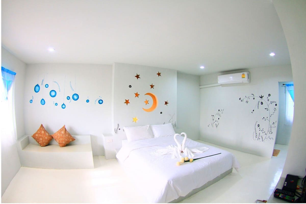 Een slaapkamer met een bed, kussens, wanddecoratie en een airconditioning.