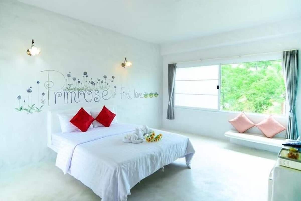 Een slaapkamer met een bed, kussens, een bloemenprint op de muur en een raam met gordijnen.