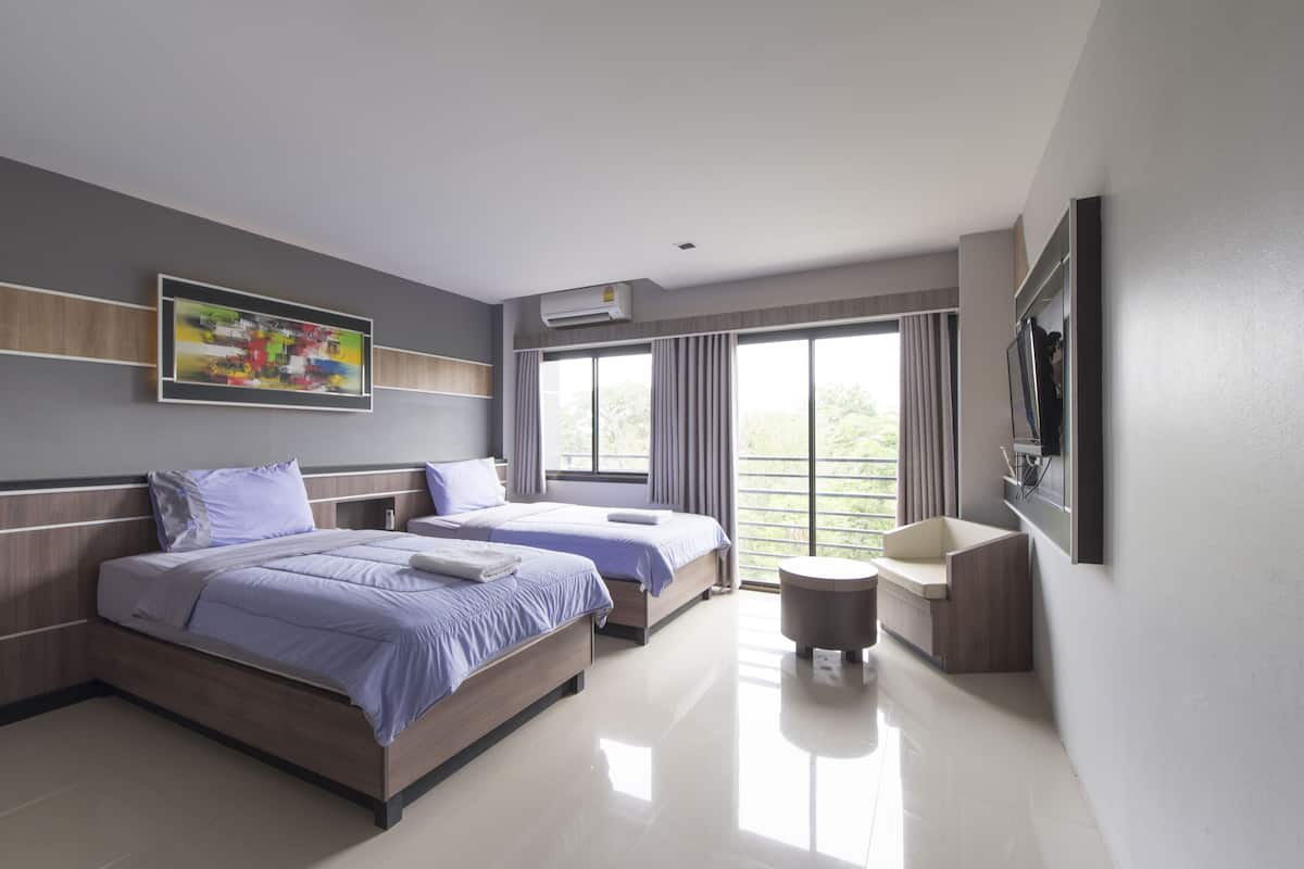 Una habitación de hotel moderna con dos camas, una mesita redonda, un televisor montado en la pared y un ventanal con cortinas.