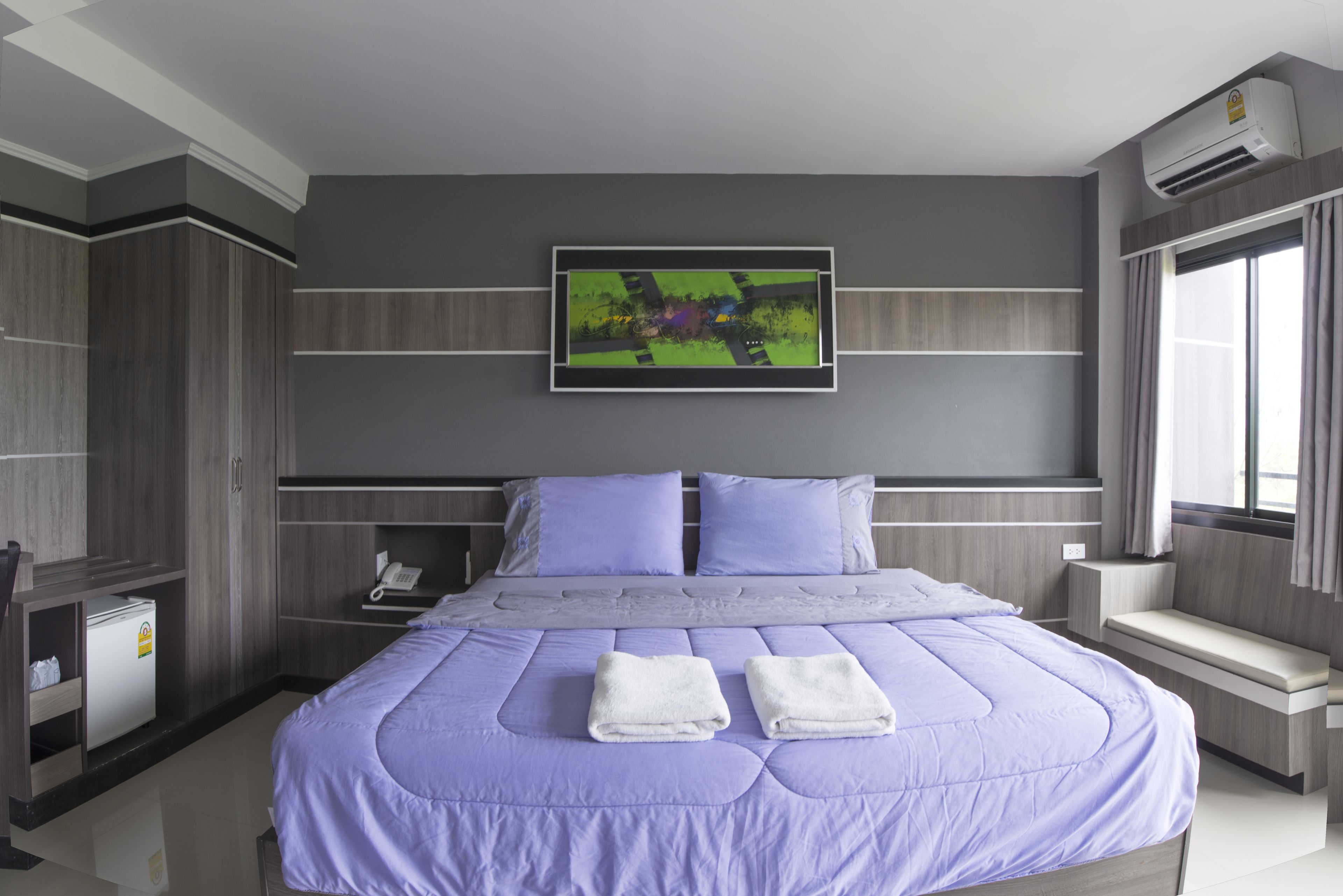 A modern hotel room with a large bed, a flat-screen TV mounted above the bed, a built-in desk, and a window with curtains.