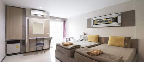 A modern hotel room with two beds, a desk, a chair, and a small kitchenette.