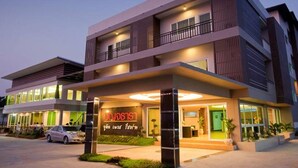 Un hotel moderno con una estructura de dos pisos, entrada cubierta y un cartel con texto tailandés.