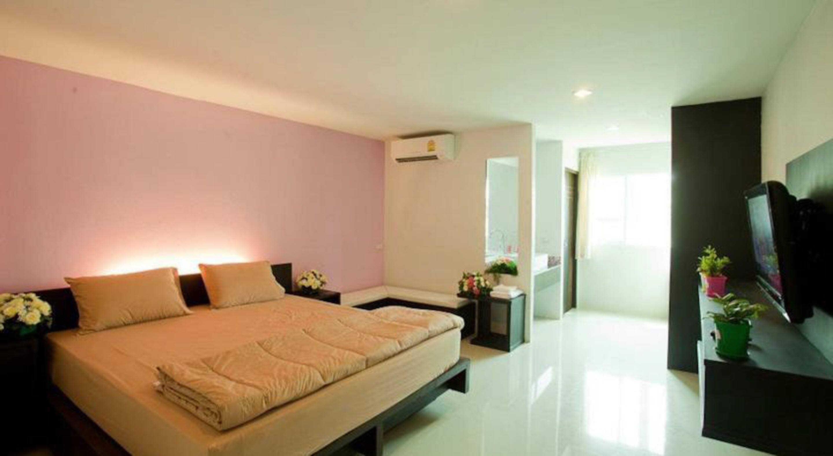 A modern bedroom with a large bed, bedside tables, a TV, and a small balcony with plants.
