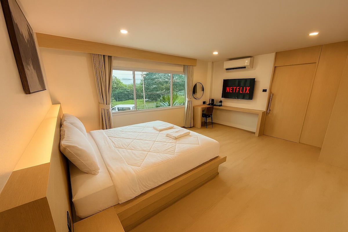 Un dormitorio moderno con una cama grande, un escritorio, un televisor y vistas al exterior con vegetación.
