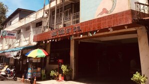 A hotel with a large mural of a rooster on the facade, a red sign above the entrance, and a tiled sidewalk. - Nett Hotel (Lop Buri)