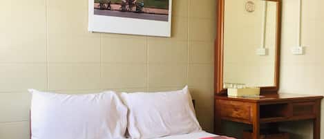 A hotel room with a bed, a wooden nightstand, a mirror, and a wall-mounted picture of a temple.