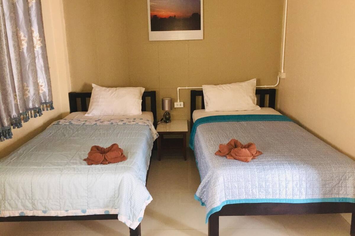 A room with two beds, each with a pillow and a folded towel. There is a picture on the wall above the beds.
