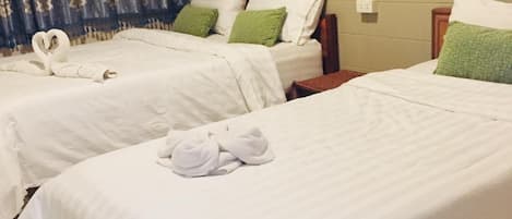 A hotel room with two beds, each with white linens and green pillows. There is a chandelier hanging from the ceiling.