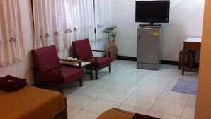 A hotel room with a bed, two red armchairs, a small table, a television on a cabinet, and a potted plant. - Nett Hotel (Lop Buri)