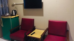 A small room with two red chairs, a small table, a television mounted on the wall, and a green cabinet with a kettle on top. - Nett Hotel (Lop Buri)