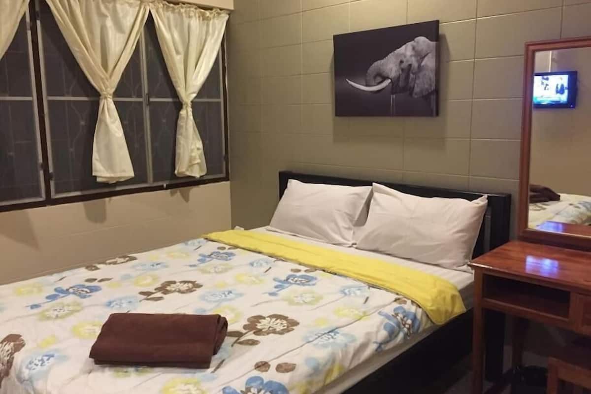 A hotel room with a bed, a nightstand, a mirror, a window with curtains, and a wall-mounted picture of an elephant.
