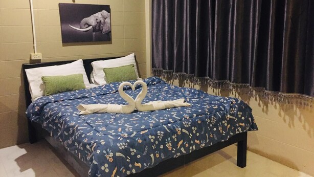 A hotel room with a bed featuring a blue floral bedspread and a swan-shaped towel arrangement. - Nett Hotel (Lop Buri)