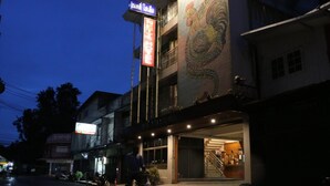 A hotel with a large rooster mural on the facade, a neon sign, and a staircase leading to the entrance. - Nett Hotel (Lop Buri)